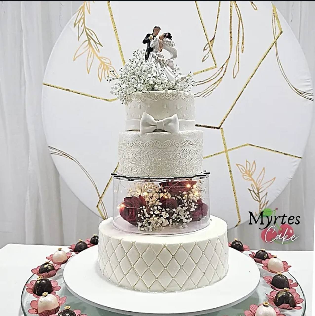 Bolo branco de andares da Myrtes Cake, com laço, renda, flores e topo com casal.
